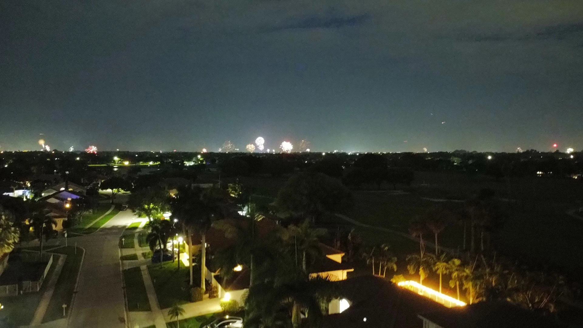Nighttime aerial view of a neighborhood with fireworks on the horizon